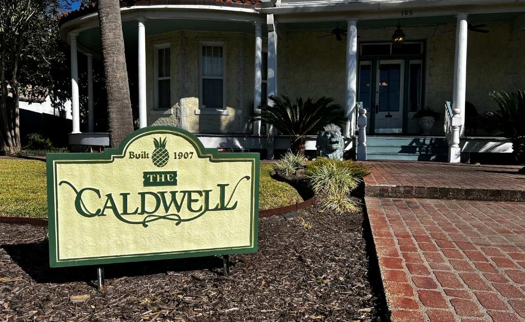 Sign for The Caldwell House Bed and Breakfast in Abbeville, Louisiana, set along the brick walkway leading to the historic front porch.