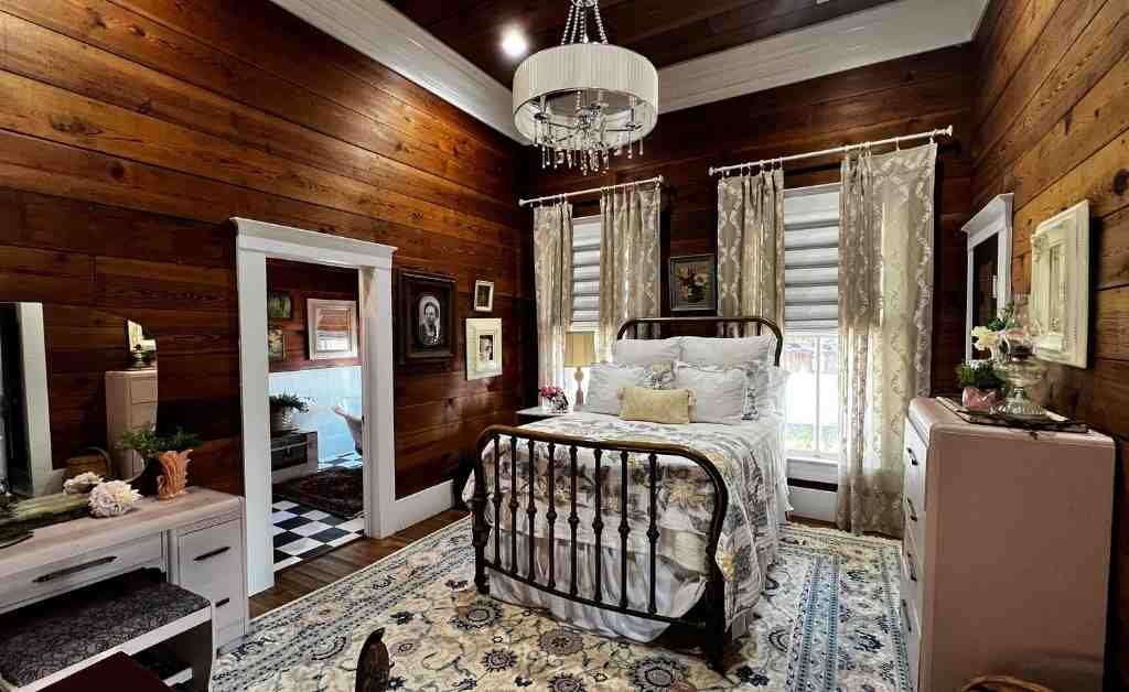 Bedroom at the Dover House in Florien with an iron bed, tall windows, and wood-paneled walls